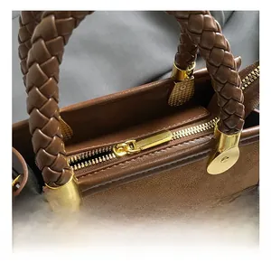Detail of woven brown leather handles and golden metal hardware on a leopard square bag