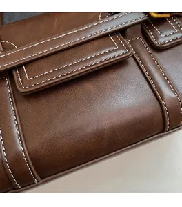 Detail of brown vintage leather bag showing white contrast stitching and bronze buckle