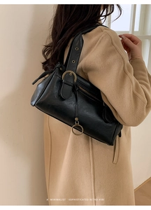 Gros plan d'un sac à bandoulière rétro noir minimaliste en cuir brillant avec boucle métal