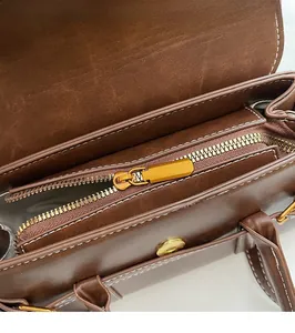 Detail of gold metal zipper and white stitching on brown leather handbag interior