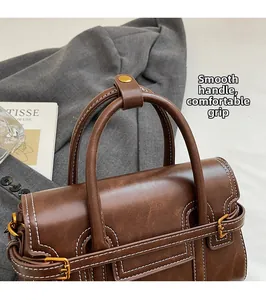 Detail of rounded brown leather handle with white stitching and gold hardware