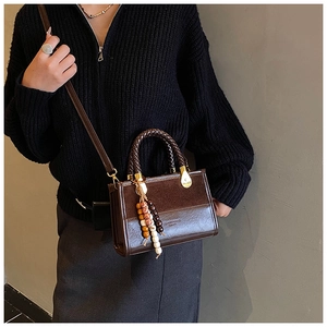 Detail of dark brown leather crossbody bag featuring braided handle and ethnic wood beads