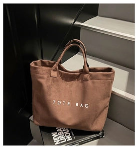 Detail of a large brown suede tote bag with letter print on industrial stone stairs