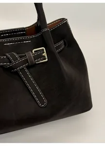 Detail view of contrast white stitching and metal buckle on dark suede tote bag