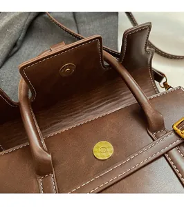 Detail of dark brown leather handbag featuring gold magnetic buckle and white stitching