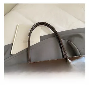 Detailed close-up of dark brown glossy leather tote bag handles with neat stitching