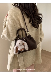 Detail of dark brown faux suede bucket bag with plush rabbit charm and gold buckle