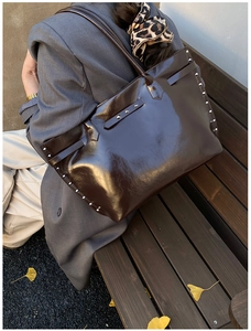 Detail of dark brown glossy tote bag with silver studs and buckles on a model