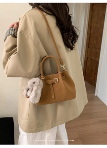 Brown matte faux leather bucket bag shown on shoulder with a plush rabbit charm accessory