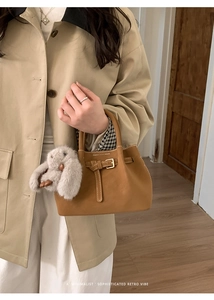 Detail of retro brown leather bucket bag with signature stitching and plush rabbit charm
