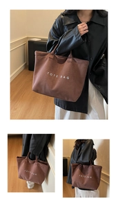 Detail view of large brown canvas tote bag featuring white TOTE BAG lettering and sturdy handles