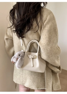Close-up of cream-white mini tote bag with leather buckle and plush rabbit keychain