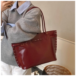 Detail of burgundy tote bag with metal rivets and glossy leather texture on shoulder