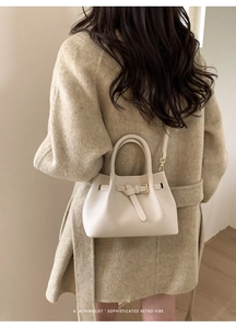 Minimalist beige handbag styled with a wool coat showing knotted strap and gold buckle