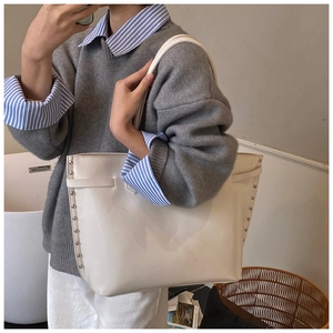 Close-up of white leather tote bag with silver rivet details shown in a casual setting