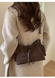 Details einer dunkelbraunen Wildleder-Schultertasche mit Kontrastnaht auf beigem Mantel