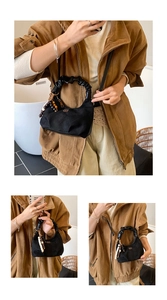 Detail of black quilted dumpling bag featuring pleated handle and beaded charm accessory