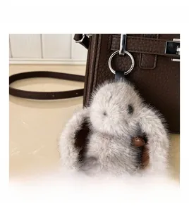 Detailed macro view of a grey plush bunny charm attached to a dark brown leather tote bag