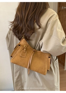 Detail einer braunen Wildleder-Schultertasche mit weißen Nähten und Lederanhänger