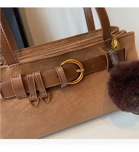 Detail of brown litchi pattern leather bag featuring gold buckle and plush ball charm