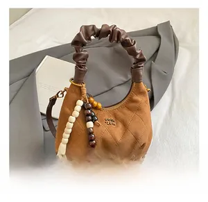 Detail of brown suede dumpling bag featuring quilted pattern and beaded charm accessory