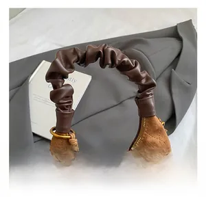Detail of a brown suede dumpling bag with diamond stitching and decorative wooden beads