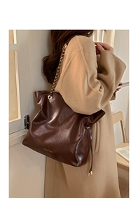 Détail du sac cabas en cuir marron brillant avec chaîne dorée et texture plissée douce
