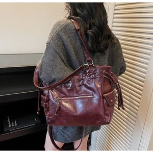 Détail du sac cabas en cuir brillant bordeaux avec œillets et rivets sur maille grise