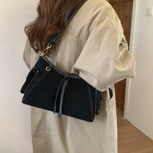 Detail of black suede shoulder bag with white contrast stitching and gold metal hardware