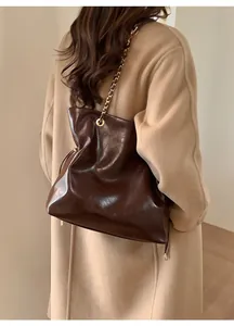 Détail du sac cabas en cuir marron foncé avec chaîne dorée porté sur un manteau beige