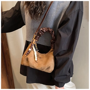 Detail view of brown faux suede dumpling bag with quilted texture and beaded charm accessory