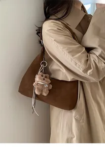 Detalle de bolso tote de ante marrón con colgante de oso de peluche y collar perlas