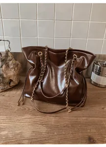 Détail d'un sac cabas en cuir marron brillant avec chaîne dorée et cordon serrage