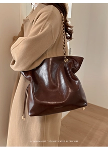 Detail of dark brown glossy tote bag with gold chain strap and elegant texture