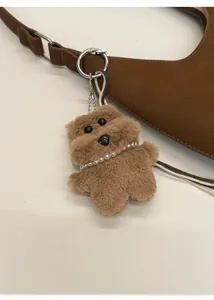 Llavero de perro de peluche marrón con collar de perlas en un bolso tote de ante