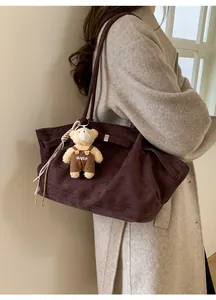Detail of dark brown suede tote bag with metal hardware and cute bear charm accessory