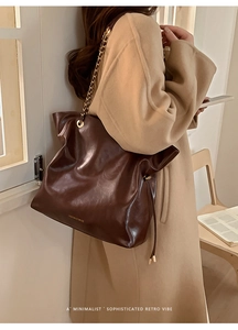 Detail of dark brown wax leather tote bag with gold chain strap on model shoulder
