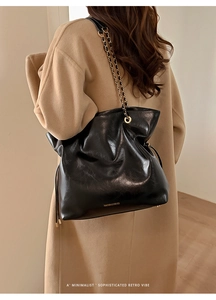 Detail of black leather tote bag featuring gold chain strap and minimalist branding