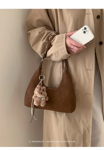 Detalle del bolso hobo retro de ante marrón con un colgante de oso de peluche y collar perlas