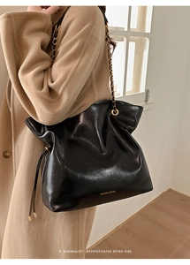 Vue détaillée du cabas en cuir noir avec bandoulière en chaîne dorée et logo gravé