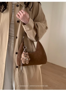 Brown hobo shoulder bag with plush bear charm and pearl chain accessory on a trench coat