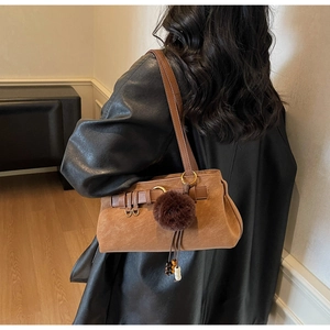 Detailed side view of a brown suede shoulder bag with a stylish pompom charm accessory