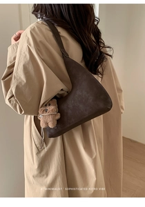 Detalle de un bolso hobo marrón oscuro con colgante de osito en una modelo