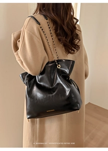 Detail of a large vintage black glossy leather tote bag with a golden chain shoulder strap