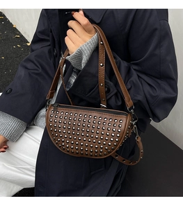 Close-up of a brown leather crescent bag with silver rivet details worn by a model