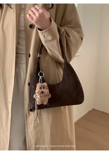 Detalle de bolso hobo marrón oscuro con colgante de osito sobre una gabardina caqui