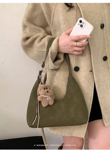 Detalle de bolso medialuna de ante verde oscuro con un tierno colgante de osito