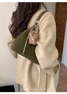 Detalle de bolso tote de ante verde oliva con colgante de oso sobre abrigo beige