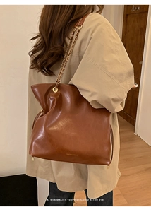 Détail d'un sac cabas marron en cuir avec chaîne dorée et texte de la marque