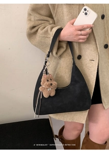 Detalle del bolso hobo negro de ante con colgante de cachorro y correa de cuero fino
